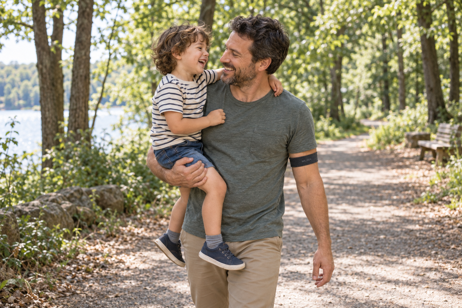 A father wearing a discreet Mura band carrying his laughing child through a leafy park